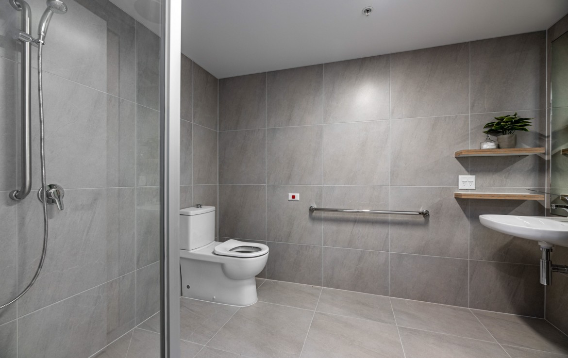 Bathroom in SDA accommodation in Moonee Ponds showing tiled floor and walls with handrail and toilet