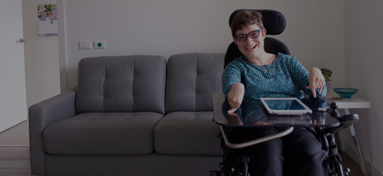 NDIS participant smiling with iPad in SDA accommodation.
